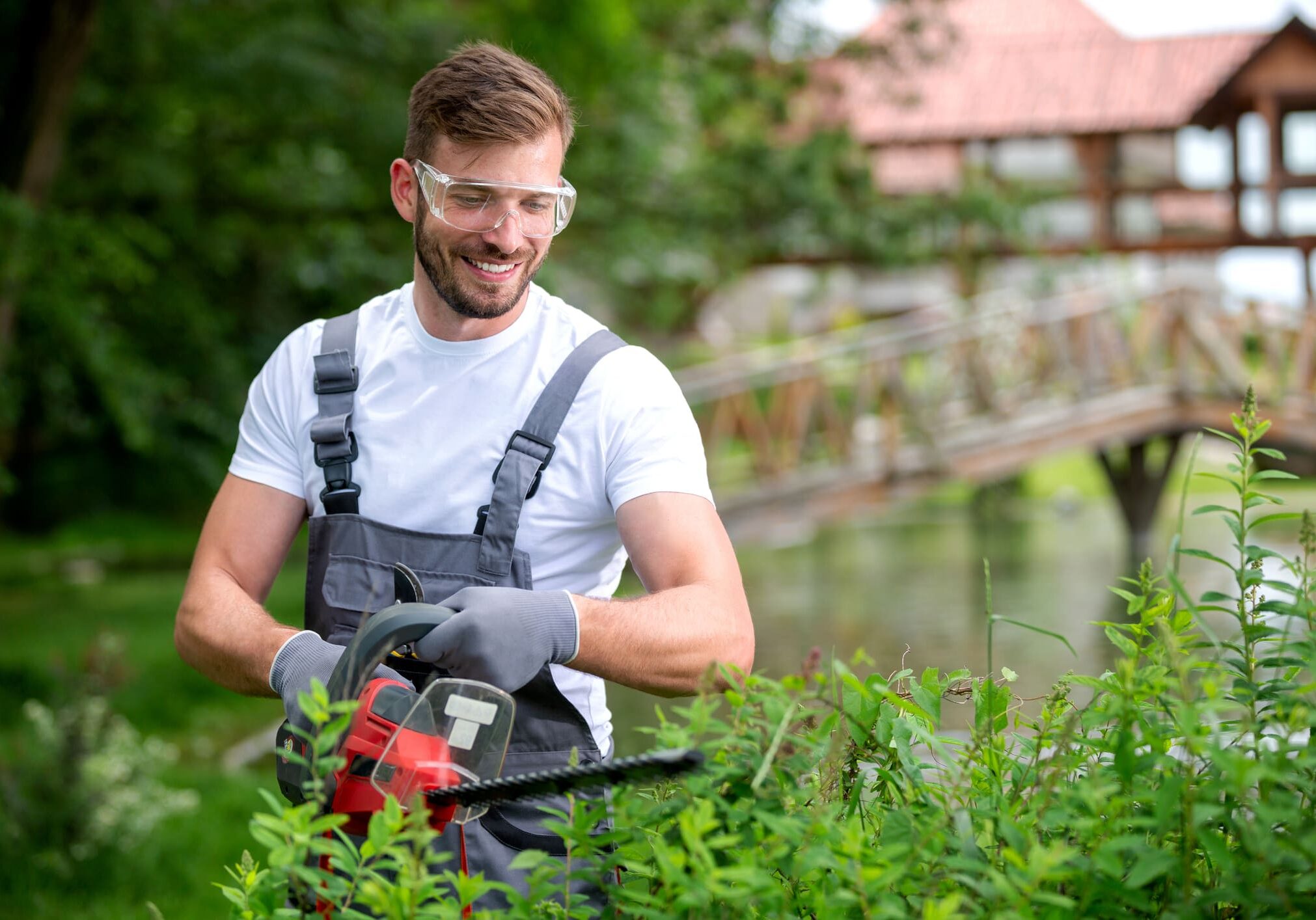 Man trimming bushes with a hedge trimmer.