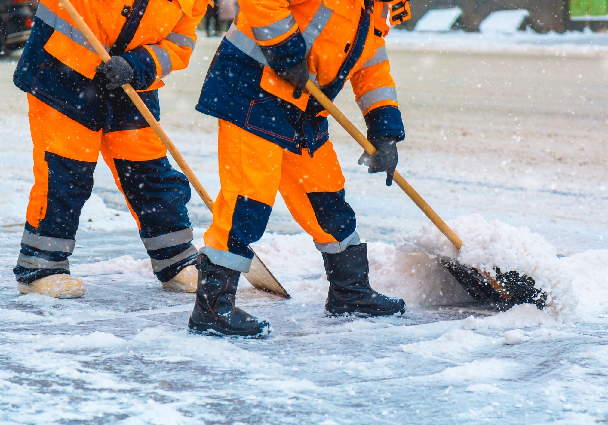 Workers shoveling snow in bright orange gear.
