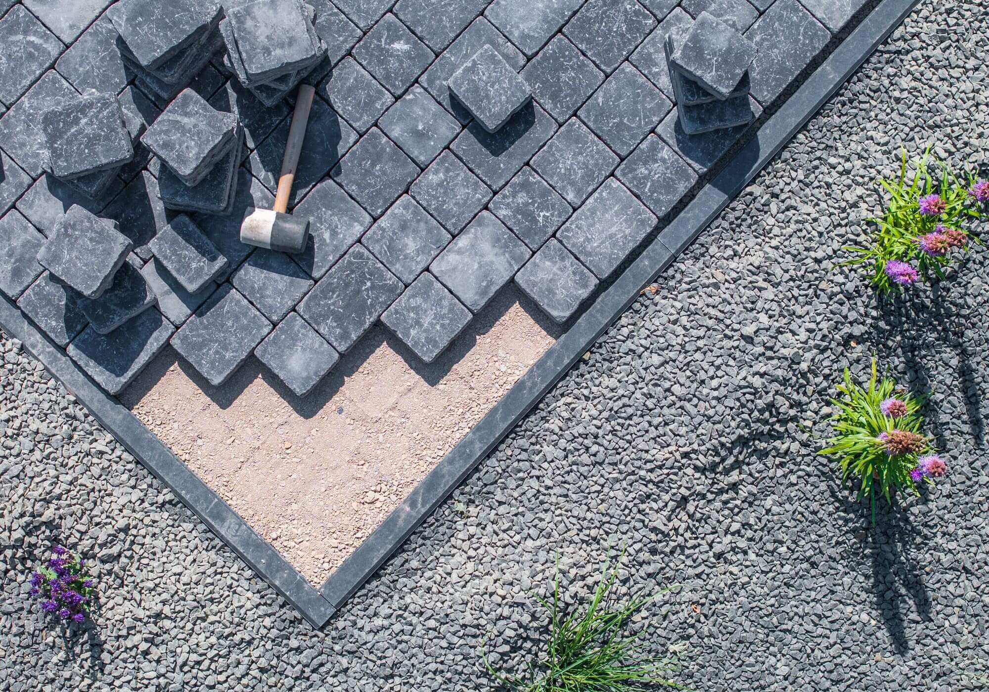 Paving stones and mallet on gravel surface.