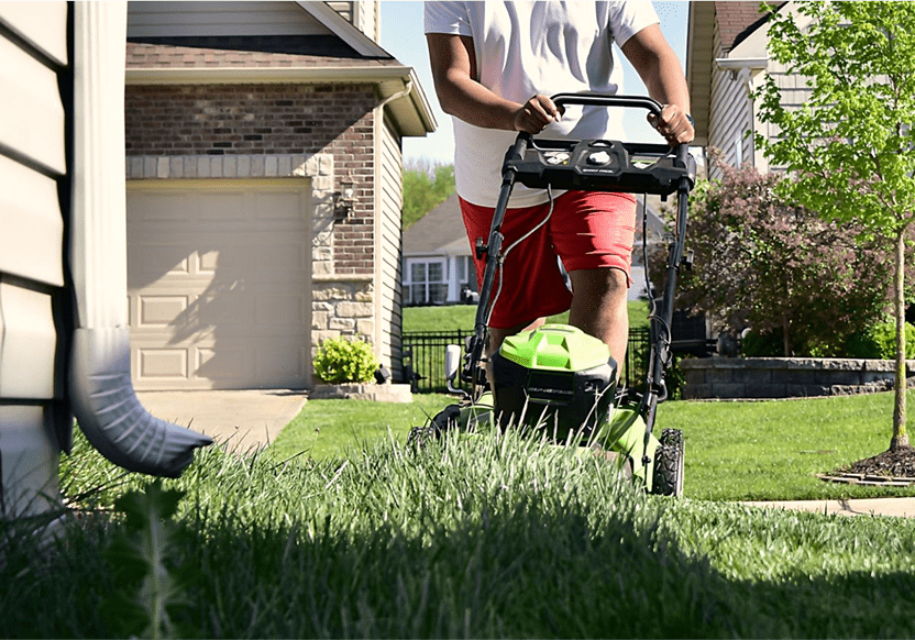 Person mowing lawn with electric lawnmower.